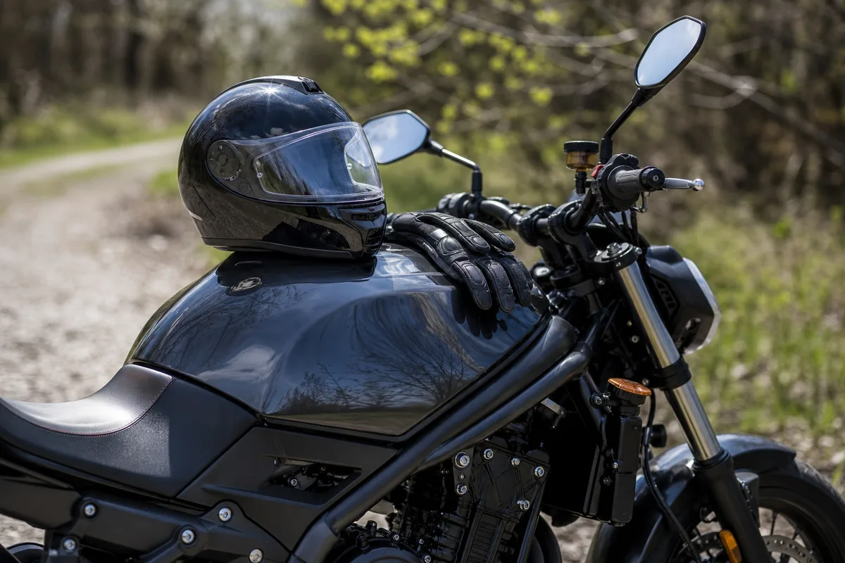 Casque intégral et gants posés sur le réservoir d’une moto garée dehors au printemps